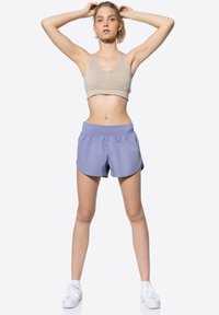 Soutien-gorge de sport beige avec un encolure dégagée et un détail froncé, associé à des shorts légers lavande dotés d'une taille élastique et d'un ourlet arrondi.