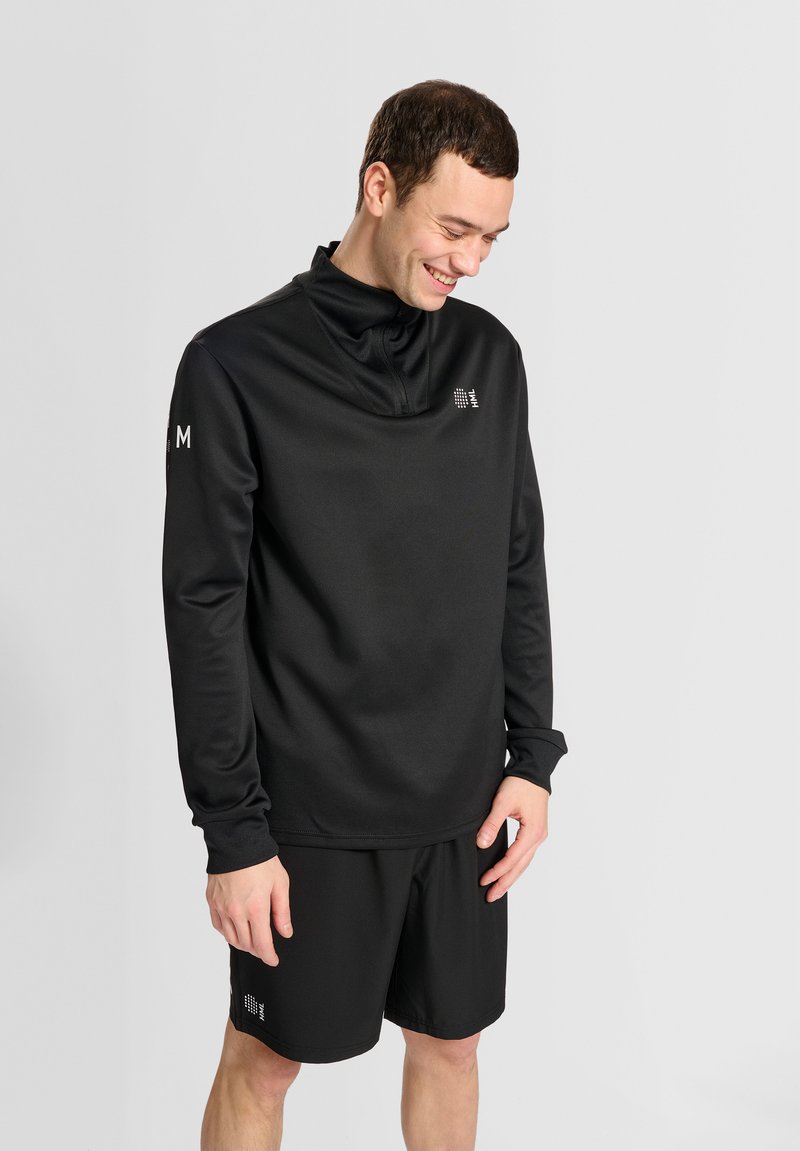 Schwarzer sportlicher Pullover mit hohem Kragen, langen Ärmeln und Logodetail auf der Vorderseite. Kombiniert mit schwarzen Shorts, aus glattem Textil, bequemer Sitz.
