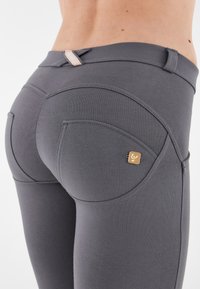 Leggings grigi con una texture liscia, caratterizzati da un design di tasche unico e un piccolo accento dorato. Vita elastica e forma aderente.