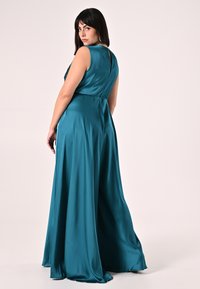 Abito in raso turchese con silhouette fluente, design senza maniche e schiena con apertura a goccia. Texture liscia con caduta leggera.