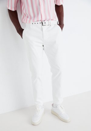 Pantalones rectos blancos de tela suave, combinados con una camisa de manga corta a rayas rosa y blanca y zapatillas blancas.