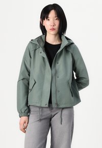 Green cropped jacket with a hood. Features front pockets, snap buttons, and drawstring at the hem. Material appears smooth and water-resistant.