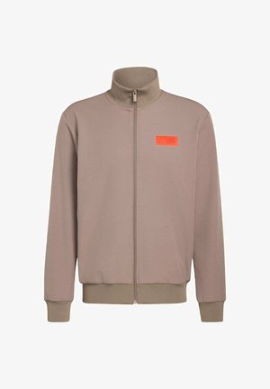 Light brown zip-up jacket with high collar, ribbed cuffs and hem, featuring an orange logo patch on the left chest. Smooth texture.