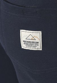 Marineblaue Stoff mit glatter Textur verfügt über ein gesticktes Etikett, das Berge und den Text "NORTHERN HORIZONS OUTDOOR UTILITY STYLE" zeigt.