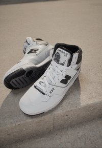 Biało-czarne wysokie sneakersy ze skóry. Charakteryzują się teksturowaną podeszwą, wyściełanym kołnierzem oraz logo na boku i języku. Model 650.