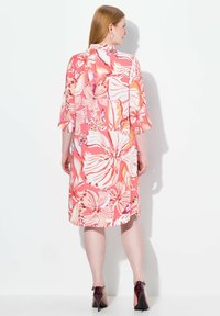 Blommönstrad klänning i rosa och orange nyanser, med ¾ ärmar och en lös passform. Baksidan har en slits och subtila sömnadsdetaljer.