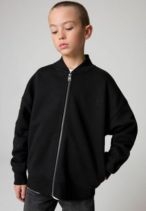 Čierna mikina na zips s vysokým golierom, s jemne embosovaným logom, vyrobená z hladkej látky s voľným strihom a rebrovanými manžetami.