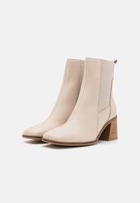 Beige Stiefeletten aus glattem Leder mit spitzem Zehenbereich, quadratischen Nähten, elastischen seitlichen Einsätzen und einem Holzblockabsatz.