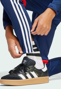 Schwarze Adidas Samba Sneaker mit weißen Streifen, marineblaue Sporthose mit weißen Seitenstreifen und gestreifte schwarz-weiße Socken.