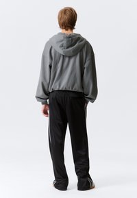 Grauer übergroßer Hoodie mit Kapuze und kontrastierender Naht, kombiniert mit schwarzen Hosen mit seitlichen Streifen und einer lockeren Passform.