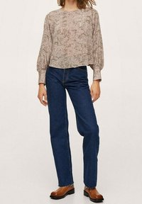 Afskåret, mønstret bluse i beige og brun, med ballonærmer, parret med blå højttaljede jeans og brune ankelstøvler.