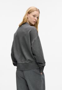 Sudadera gris de gran tamaño con dobladillo acanalado, textura suave y hombros caídos, combinada con pantalones de chándal a juego para un look cohesivo.