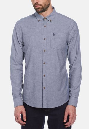 Chemise bleu clair à boutons avec une poche poitrine, boutons marron et un petit logo brodé sur le côté gauche. Manches longues et design avec col.