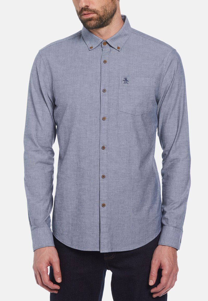 Lichtblauw overhemd met knopen en een borstzak, bruine knopen en een klein geborduurd logo aan de linkerkant. Lange mouwen en kraagontwerp.