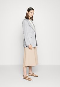 Blazer de linho cinza claro com lapelas recortadas, bolsos laterais, combinado com uma saia midi bege e sandálias bicolores castanhas. Design simples e ajustado.