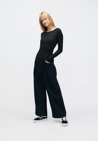 Juodas ilgomis rankovėmis viršus derinamas su tamsiais, plačiomis kojomis ir aukštu liemeniu džinsais bei juodais sportbačiais su baltais padais. Lygi ir paprasta tekstūra.