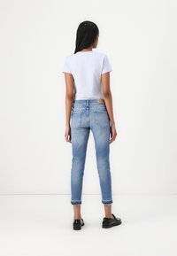 Svijetloplavi majica i iznošene svijetloplave traperice s skraćenim rubom. Model nosi crne cipele. Vidljive stražnje džepove i oznaku brenda na trapericama.