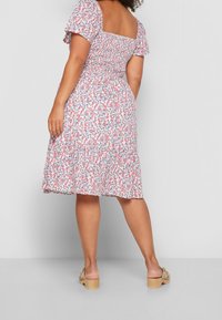 Blumenkleid mit quadratischem Ausschnitt, kurzen Ärmeln und tailliertem Oberteil, das zu einem gestuften Rock übergeht. Die Farben sind Pink, Blau und Weiß.