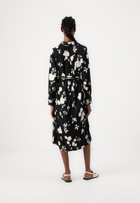 Μαύρο φλοράλ φόρεμα με λευκά σχέδια, μακριά μανίκια, ζωνάκι στη μέση και ρέουσα σιλουέτα. Φορεμένο με επίπεδες, λουριές σάνταλες.