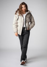 Gewatteerd jack in lichtgrijs met een afneembare capuchon, doorgestikte textuur, ritssluiting aan de voorkant, gecombineerd met zwarte jeans en sneakers met patroon.