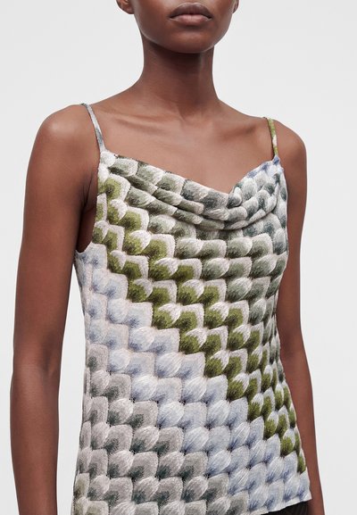 Femme portant un haut sans manches avec de fines bretelles et un motif texturé semblable à des écailles dans des nuances de vert, gris et blanc.