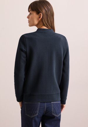 Felpa blu scuro, testurizzata, con motivo a spina di pesce, polsini e orlo a costine. Abbinate a jeans in denim scuro, viste da dietro.