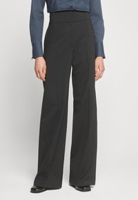 Pantaloni neri a gamba larga con vita alta, realizzati in un tessuto morbido, caratterizzati da un davanti plissettato e linee pulite e sartoriali.