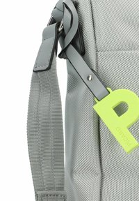 Borsa in tessuto grigio con texture e finitura riflettente, dotata di una tracolla nera con accessori metallici e un'etichetta verde brillante che mostra la lettera "P".