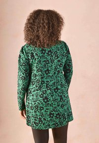 Long-sleeve tunic in green fabric with a black floral pattern, featuring a relaxed fit and gathered detail on the sleeves.