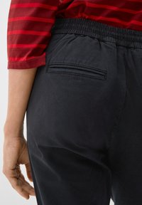Pantalon noir à taille élastique avec une texture lisse, doté d'une poche arrière, accompagné d'un haut rayé rouge et blanc.