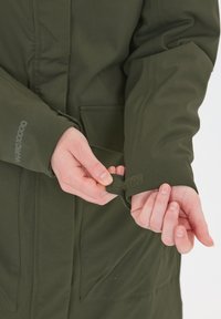 Groene waterdichte jas met een klittenband verstelbare manchette, een gladde textuur en zichtbare branding op de mouw.