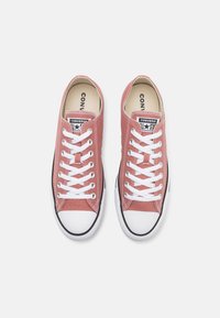 Zapatillas bajas de lona rojas con cordones blancos y suelas de goma. Presentan una franja negra, un logo de estrella y punteras.
