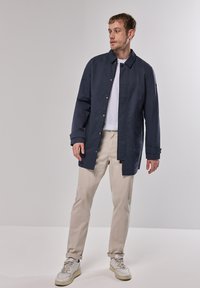 Chaqueta ligera de color azul marino con corte recto, botones de presión y mangas largas. Combinada con pantalones beige y zapatillas blancas.