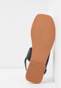 Sandale noire avec une tige texturée, dotée d'un design à bout ouvert. La semelle est marron avec un motif strié pour une meilleure adhérence.