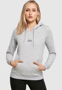 Sudadera gris con escote en V, cordones ajustables y un bolsillo frontal tipo canguro. Presenta el texto "Sunlover Starchaser" en negro.