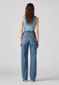 Combinaison en denim avec un buste ajusté et un pantalon large. Couleur bleu clair, bretelles réglables et deux poches arrière avec un stitching décoratif.