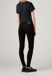 Jeans skinny negros de denim con textura suave, con una cintura de altura media y bolsillos traseros, combinados con una camiseta negra de manga corta.