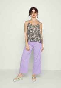 Camisola floral com alças finas, combinada com calças largas lavanda e sandálias de plataforma verdes. Corte folgado, tecido suave e acessórios mínimos.