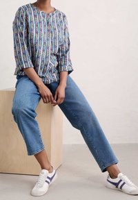 Blusa a fiori blu con collo tondo e maniche a tre quarti, abbinata a jeans blu chiaro e sneakers bianche con strisce viola.