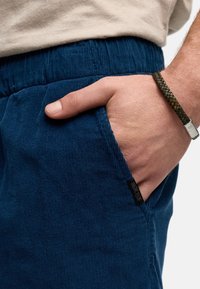 Pantalons en velours côtelé marine avec une texture ribbée, dotés de poches latérales. Une étiquette de marque noire est visible sur la poche gauche.
