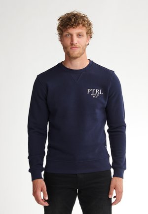 Marineblauwe sweatshirt gemaakt van een zachte stof, met een ronde hals, lange mouwen en een klein wit logo op de borst.