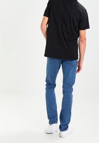 Svart kortärmad t-shirt i kombination med blå denimjeans med rak benklippning, bakfickor och vita sneakers.