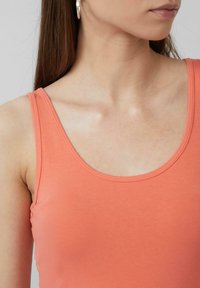 Koraalkleurig tanktop met een ronde hals en dunne bandjes; glad, rekbaar materiaal met een lichte glans; geen zichtbare patronen of hardware.