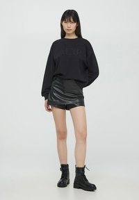 Felpa nera con testo in rilievo "AMOUR", abbinata a una mini gonna nera in pelle sintetica e stivaletti neri con lacci alla caviglia.