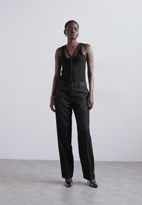 Fekete ujjatlan felső vékony pántokkal, fekete nadrággal kombinálva, amely textúrált mintával és egyenes szabású kialakítással rendelkezik. Magas sarkú cipő.