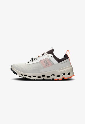 Chaussure de course avec une tige en mesh blanche, des accents noirs et des détails en orange néon. Semelle épaisse avec des découpes pour la respirabilité et l'amorti.