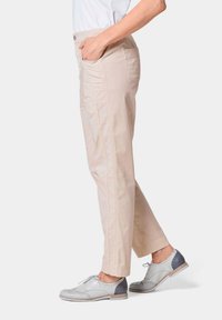 Beige katoenen broek met een recht model, zijzakken en riemlussen, gecombineerd met grijs-witte brogueschoenen. Eenvoudig ontwerp, lichtgewicht stof.