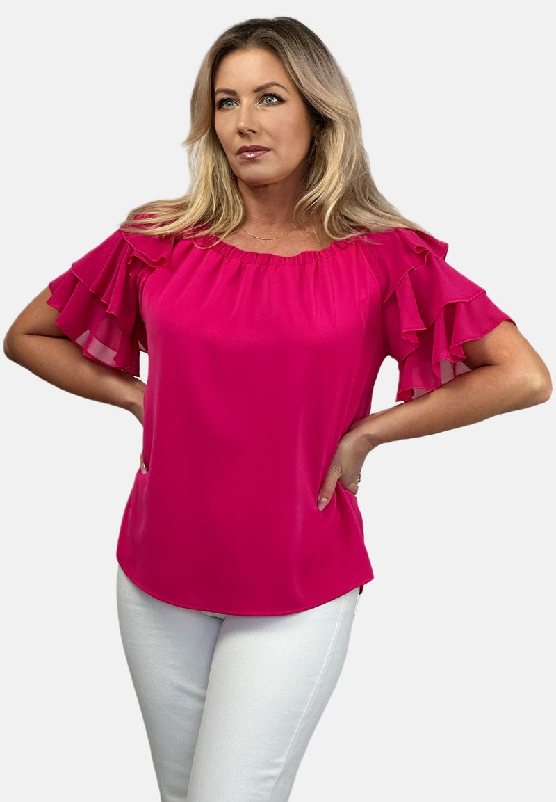 Bluzka fuksjowa z odkrytymi ramionami i falbaniaszczymi rękawami, wykonana z lekkiego materiału, w połączeniu z białymi spodniami dla kontrastu. Gładka faktura.