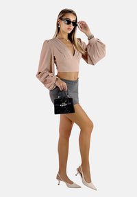Rosafarbene, langärmlige, verkürzte Bluse mit Falten, grauer, hoher Minirock, schwarze, strukturierte Handtasche und hellrosa, hochhackige Slingback-Schuhe.