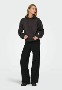 Zwarte cropped hoodie met een voorkantzak en trekkoorden, gecombineerd met ruime zwarte broeken. Soepele textuur, casual ontwerp.